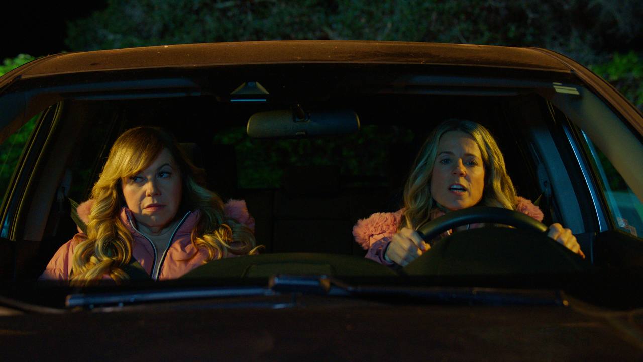 Two women ride in a car at night, one driving and the other looking concerned.