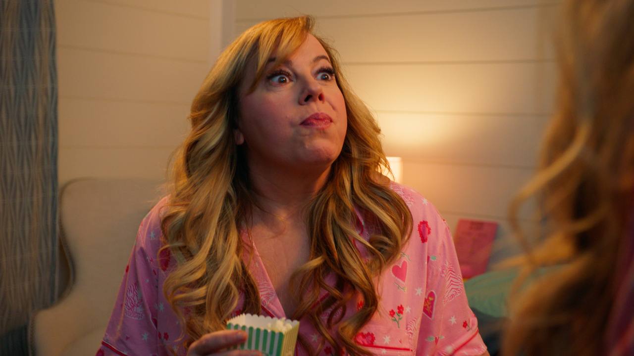 A woman in pink pajamas speaks while holding a striped popcorn cup.