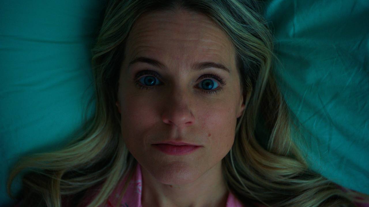 A blonde woman lies awake on a teal pillow in cool nighttime light.
