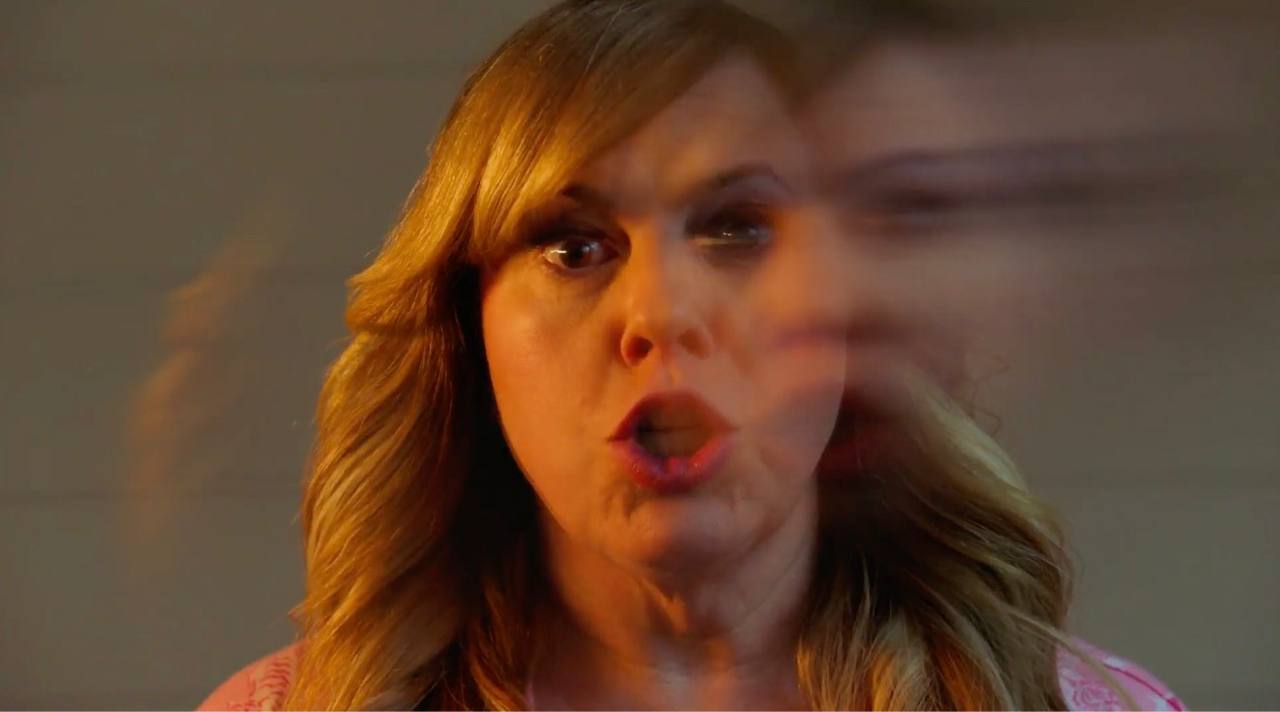 A woman in pink pajamas reacts as a blurred figure moves across the frame.