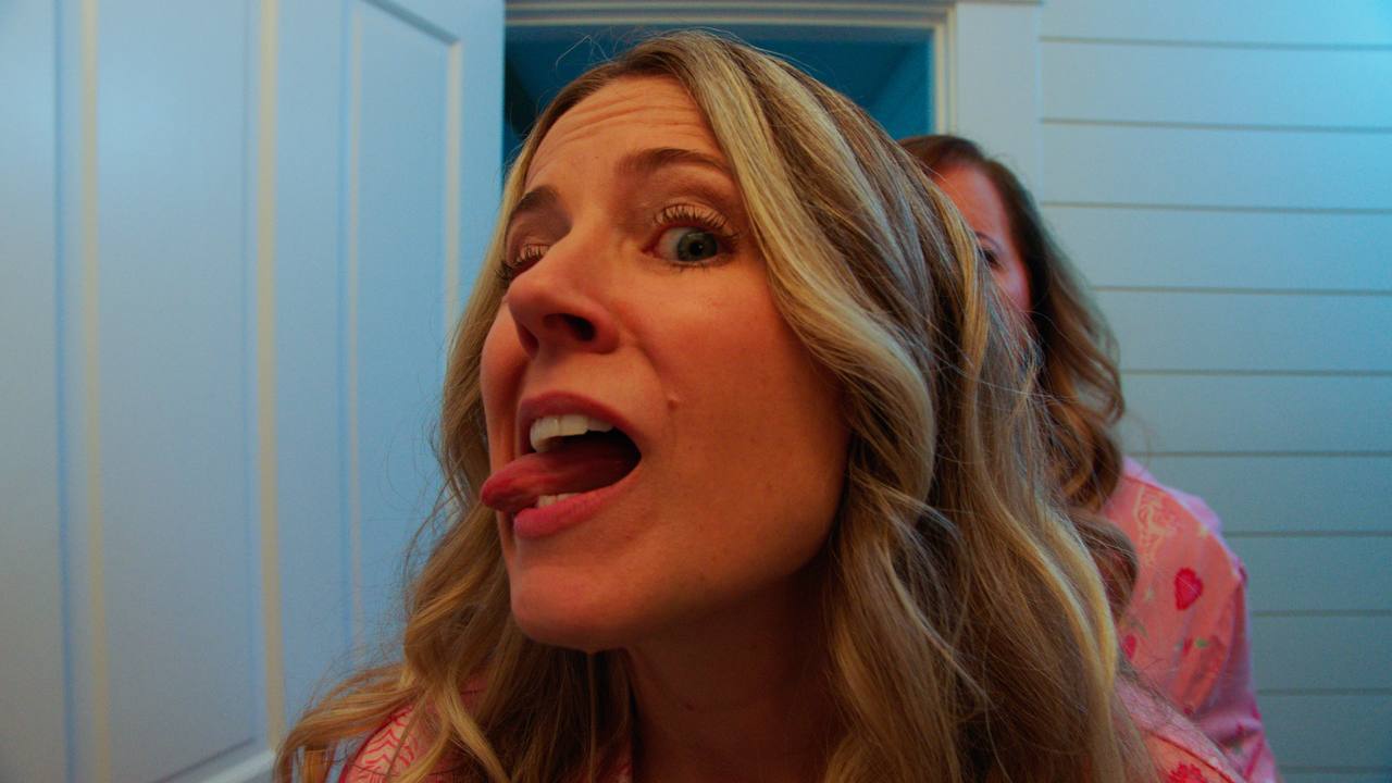 A woman in pink pajamas sticks out her tongue while another stands behind her.